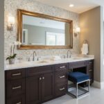 Bright bathroom with beige textured tile wall, dark wood vanity, and white countertop. Features two sinks, a large mirror, an.