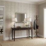 A stylish living room featuring beige patterned wallpaper, a dark wood console table with lamps, and a coat rack near a brigh.