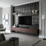 Black geometric patterned tile wall with a flat-screen TV, gold and white wall sconces, and a wooden media console in a conte.