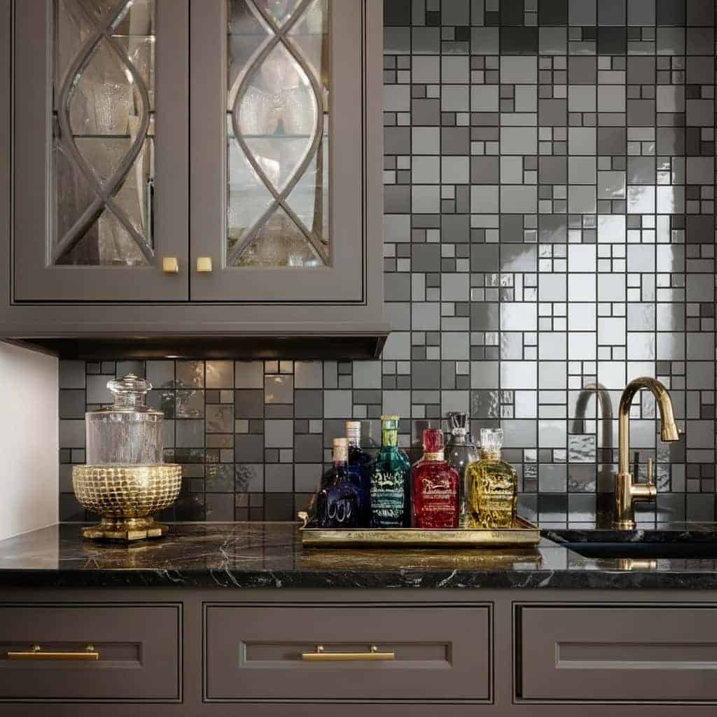 Colorful glass bottles on black marble countertop, gray mosaic tile backsplash, gold faucet.
