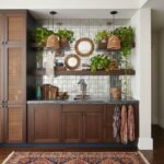 A stylish kitchen backsplash with white square tiles, complemented by wooden shelves, green plants, and decorative mirrors fo.