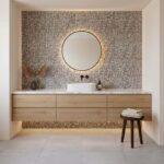 Modern bathroom vanity with mosaic tile wall, round mirror, and wooden cabinet, creating a sleek and contemporary look.