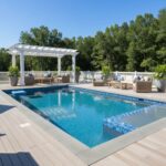 Bright blue mosaic tile pool with surrounding wooden deck and lush green trees.