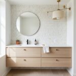 Light wood vanity with white countertop and round mirror, geometric patterned tile wall, and gold accents.
