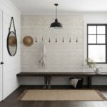 A textured white brick tile wall with black hooks, a wooden bench, and decorative accessories in a modern entryway.