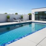 Bright blue swimming pool with smooth, light-colored surrounding tiles and contemporary lounge chairs.