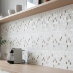 A close-up of a beige mosaic tile wall featuring small square accents and a textured surface, ideal for kitchen or bathroom b.