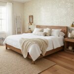 A cozy bedroom with a textured, neutral-colored wallpaper, wooden furniture, and soft bedding creating a warm, inviting atmos.