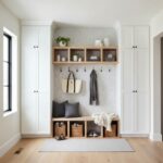 Bright entryway with white cabinets, wooden shelves, and hooks for organization. Neutral tones and natural materials create a.