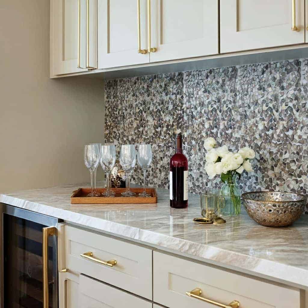 Elegant marble tile backsplash with a mix of gray, white, and beige tones, complemented by gold accents on cabinet handles.