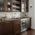 Elegant wood kitchen cabinet with glass-front upper doors and a built-in wine cooler. Features a dark wood finish, gold handl.