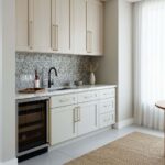 Bright white kitchen cabinets with gold handles and a mosaic tile backsplash.