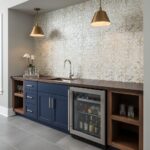 Bright mosaic tile wall with subtle beige and cream tones behind a navy blue kitchen cabinet and wine cooler.